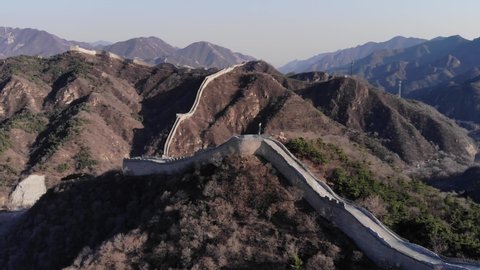 Long chain of Great Wall of China running at mountains range, aerial view at early spring season. Distant areas of famous Badaling site, reconstructed main structure with some parts of parapet missing