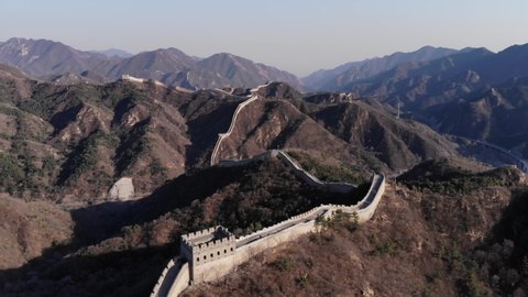 Badaling Great Wall of China, stone strip of fortifications run far away on hills and mountains. Scenic aerial shot at early spring time. Watchtower building at front, mountainous area on background