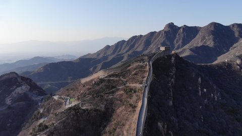 Scenic aerial shot of steep Great Wall of China at Badaling section. Tourists climb around popular landmark. Watch tower on top of hill, big mountains on background