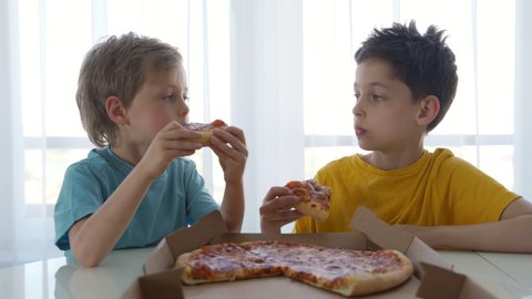 Two little caucasian boys eating pizza at home. Day light.