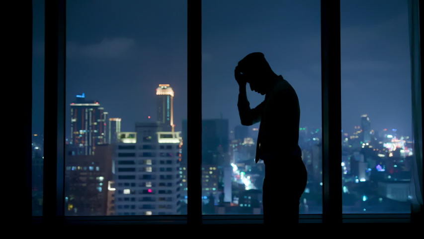 Silhouette of upset businessman standing by the window at night | Shutterstock HD Video #1032237152