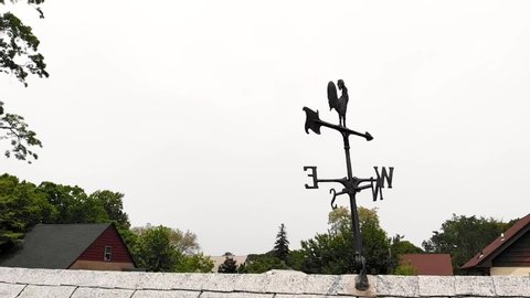 Aerial view of weather vane on top of garage roof with trees and overcast sky in background.