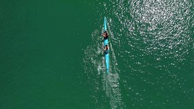 Aerial drone top view video of sport canoe operated by 2 young fit athletes in tropical lake with clear water
