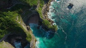 Bali - Bukit peninsula. Aerial footage of transparent turquoise ocean and rocky cliffs, covered with tropical trees.