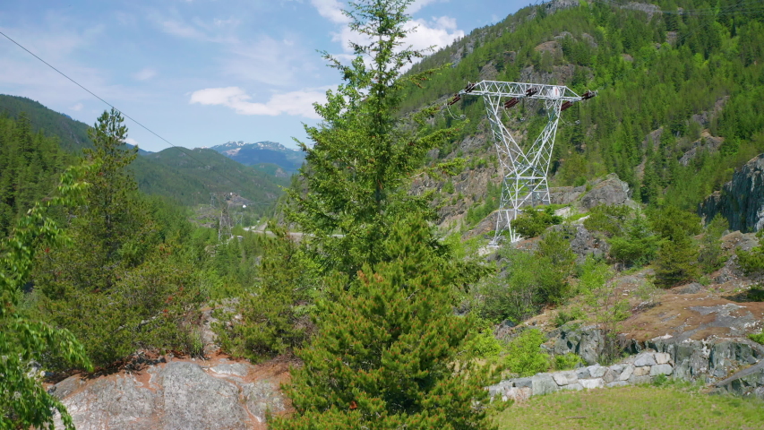Aerial drone view rising above the trees to reveal a highway and powerlines running through the mountains