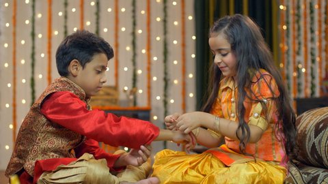 Cute sister celebrating Raksha Bandhan with her sweet little brother - festive season . Pretty little sister tying rakhi as a symbol of love, care and respect on her brother's wrist