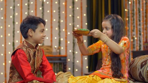 Smiling and cute young Indian siblings celebrating Raksha Bandhan / Bhai Dooj traditions - festival concept . Cute little sister doing aarti / pooja of her brother on the occasion of rakhi / tika