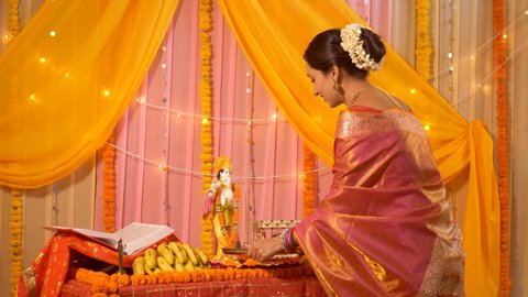 Indian woman performing Pooja, worshiping Lord Krishna - Hindu ritual and customs. Indian stock video of a beautiful woman wearing saree and doing aarti for Gopala Krishna's idol - Krishna Janmashtami