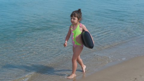 The child walks on the beach. Happy little girl in a bathing suit walking along the seashore.