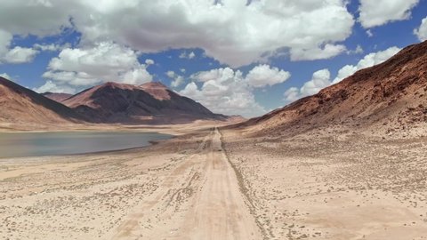 Aerial over off road 4x4 car driving along gravel trail path near arid desert mountains.Pamir Highway silk road trip adventure in Kyrgyzstan and Tajikistan desert,central Asia.4k drone flight video