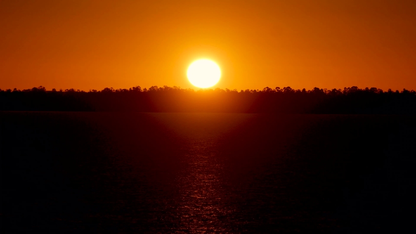Orange sunset, being reflected in a lake. The image is in long shot and blurred background