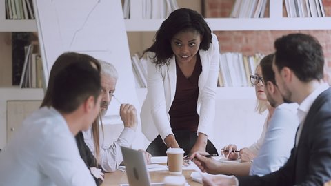 Serious african american female business leader talking at diverse group meeting, confident black boss manager instructing workers team presenting financial report planning work at group briefing
