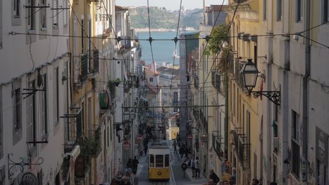 LISBON, PORTUGAL - APRIL 31, 2019: Retro yellow tram running down the lively narrow street. Tramway system in operation since 1873