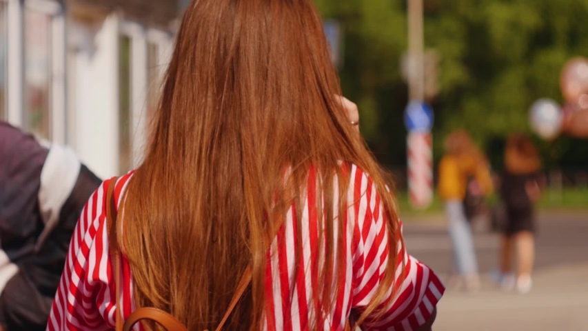 Young woman with long hair walking on the street center and talking phone. Medium shot.