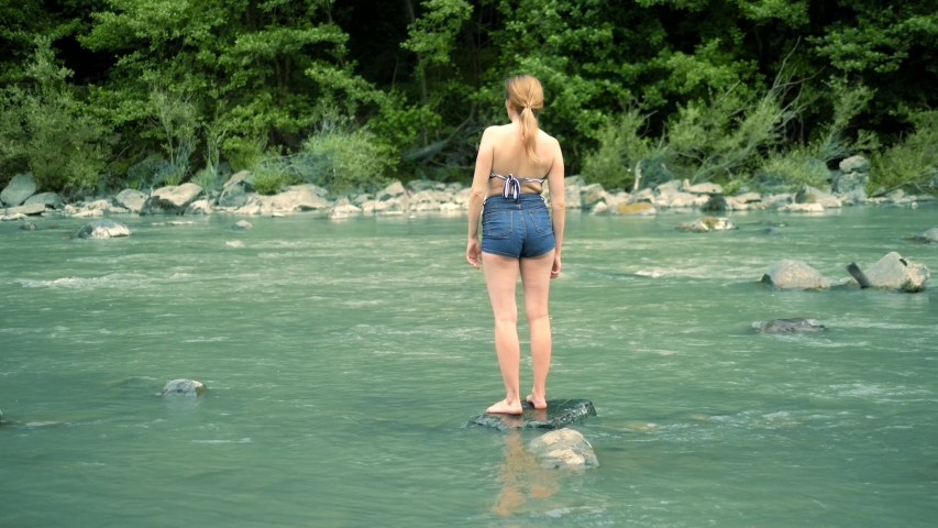 summer holiday concept. a woman in a bathing suit and shorts goes over a mountain river to a ford