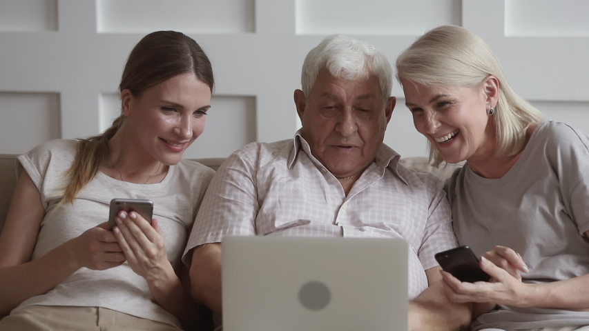 Happy family old senior retired parents and young daughter using laptop phones at home talking laughing sit on sofa having fun with devices together, age generations and technology addiction concept | Shutterstock HD Video #1032303689