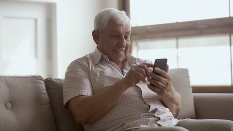 Happy elder senior man holding smartphone using mobile online app, smiling old aged grandpa texting sms message 