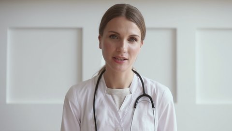 Young professional woman doctor wear uniform with stethoscope talk by conference video call chat consult patient online looking at camera webcam, distant medical consultation in internet app concept