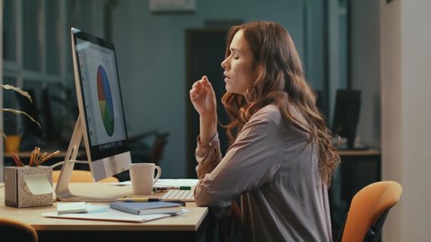 Upset business woman looking at financial report on computer in office at night. Nervous female professional finding mistake in charts at evening office. Shocked woman working overtime with documents.