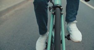 Cyclist guy riding fixed gear sport bike in sunny day on city. Hipster man in casual summer cloths and bicycle on street. Front tracking close-up of wheels. 4K slow motion raw video footage 60 fps