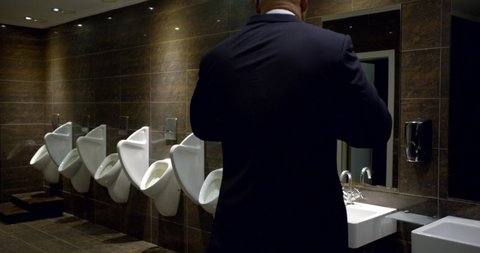 adult bald businessman is entering in toilet room in restaurant, using urinal