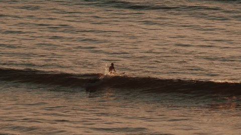 Two surfers in the water during sunset in slow motion. One catches a small wave.
