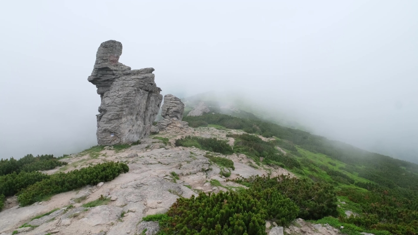 Summer mountain ridge with big vertical stony rocks. Wind with low clouds and fog. Carpathian, Chornohora, Vuhatyj Kaminj, Ukraine.
