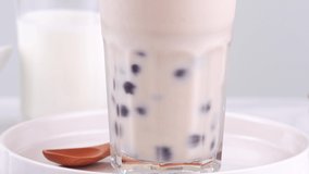 Stirring tasty taiwanese popular drink tapioca pearl bubble milk tea in glass cup on bright marble table white tray, homemade concept. 4K shot video