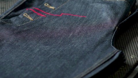 Stunning slow motion close up shot of denim lasers artificially imprinting worn patterns on to new jeans.