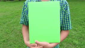 Young cute white kid holding green big papaer book in hands with empty blank cover. Child pointing at book with index finger and gives thumb up as symbol of like and success.