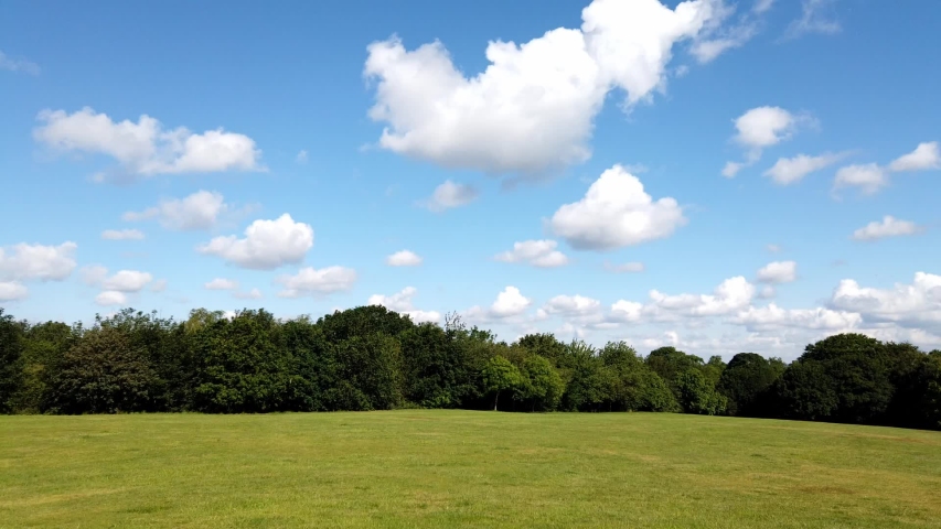 Timelapse clouds forming above open park, dog walkers walking quick pace through scene across grass.