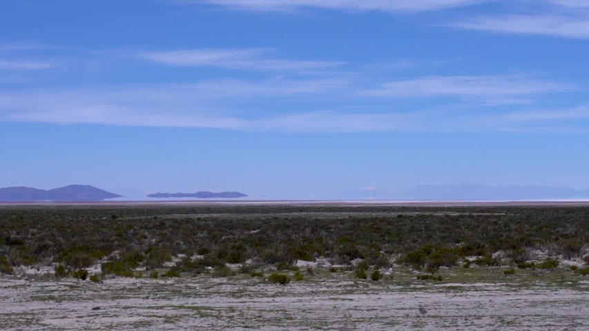 Mirage and heat reflections, desert, mountains, clear blue sky and green fields as seen from train in slow motion, Salar de uyuni salt flats in Bolivia, Latin america