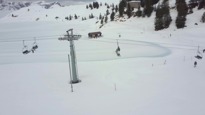A side on drone view of skiers sitting in a ski lift in the Alps.