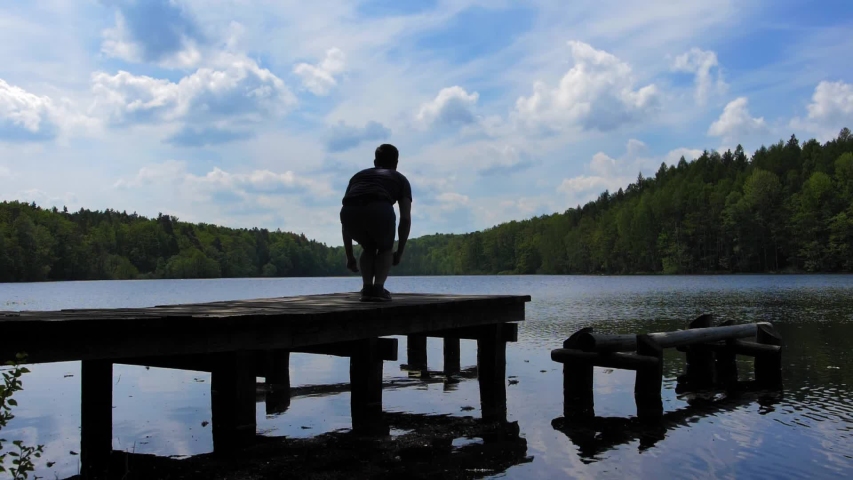 Happy Young Male Silhouette Jumping Up on Wooden Jetty on Lake