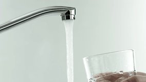 in the video, a water tap, water runs, hand brings a glass tumbler to the tap, the glass is completely filled with water, hand carries the glass, white background