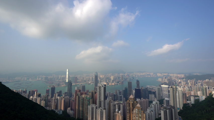 View from high above beautiful Hong Kong looking down a lush green valley from a hilltop overlooking the city. Tall skyscrapers fill the horizon in this busy Asian destination. TILT DOWN.