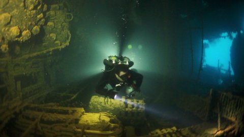 Diver on sunken ship inside view on wreck underwater in Truk Lagoon on Chuuk Islands. Shipwreck in historic place of terrible tragedy of WW II and diver among wreckage of ship.