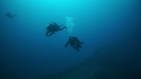 Divers near shipwreck in underwater submarine world of ships from World War II as result of military battles on Truk Islands. Concept of diving in historic underwater sites of sunken wreck.
