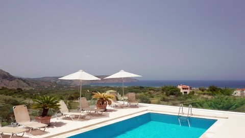 Low Aerial Flyover of Luxury Greek Villa Patio & Loungers revealing Coastline in the Distance in Crete, Greece