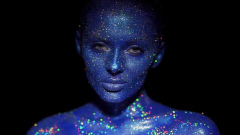 Portrait of beautiful woman with blue sparkles on her face. Girl with art make-up in color Light. Fashion model with colorful makeup