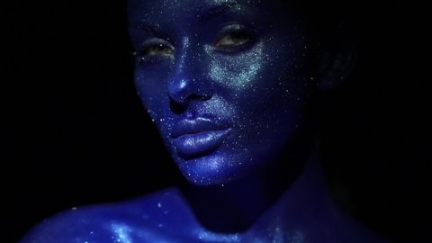 Portrait of beautiful woman with blue sparkles on her face. Girl with art make-up in color Light. Fashion model with colourful makeup