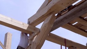 Workers build and stack boards wooden house. Clip. Workers install beautiful wooden beams on construction site of house. Wooden house in mode of construction on background of sky