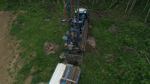 Overhead panning aerial view of water well drilling rig operator adding an additional length of pipe.