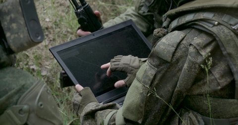 Soldiers in camouflage in ambush, military engineer uses a laptop navigation system, military action in the steppe area.