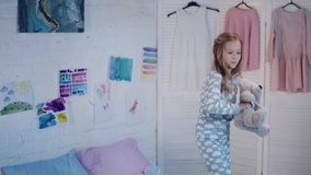 happy kid in pajamas holding teddy bear and jumping on bed in bedroom