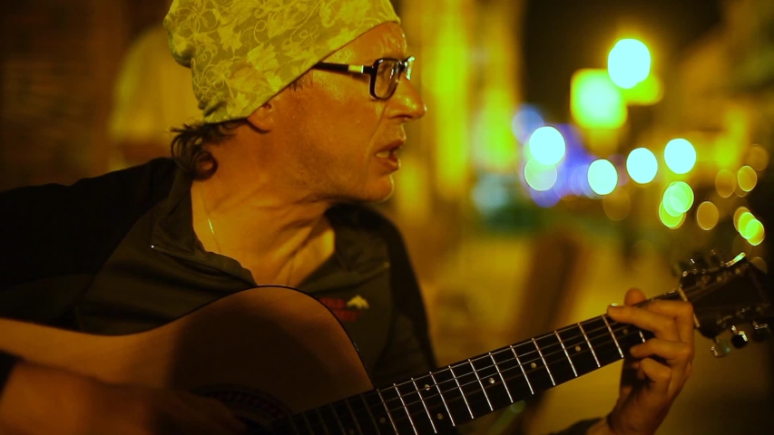 Adult male Street Musician Plays Guitar In The Street At Night.