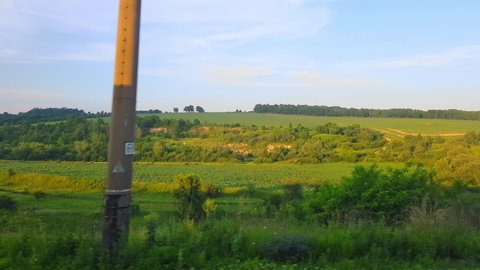 The view from the high-speed train on the beautiful scenery with hills and forest before sunset. The view from the window of the car, bus, train. Journey from the train on a sunny day