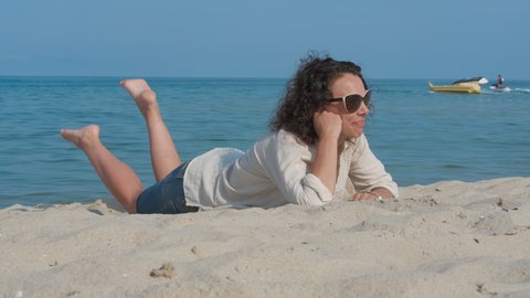 Happy woman is lying on the sand at the beach.