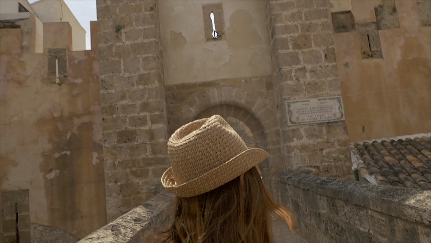 A young woman tourist rear view walking into a medieval castle in Spain in a small city of Bunyol or Bunol near Valencia  famous for Tomatina event. Woman in a cute summer dress is enjoying holidays.