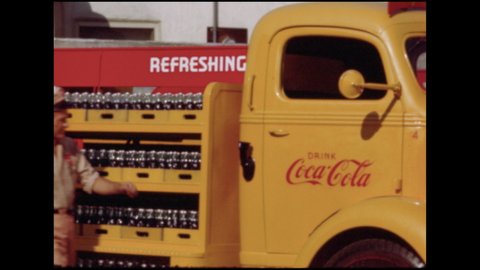 1950s: A man drives a truck loaded with Coca-Cola bottles The Coca-Cola truck makes a turn and several cases of Coca-Cola fall off the truck and break. The truck bumps into car in front of it.